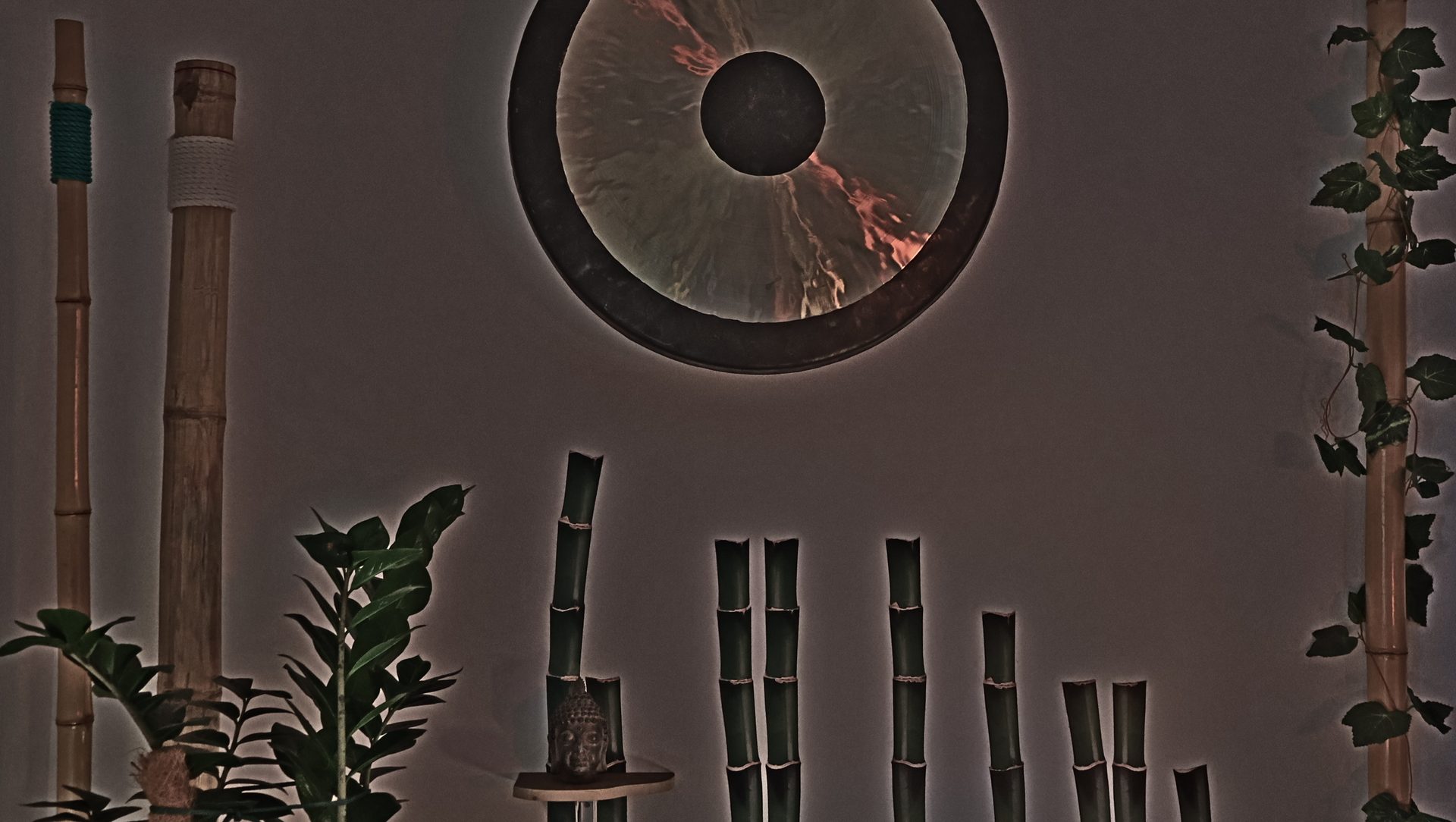 A large gong lit on the studio wall, above bamboo and a Buddha head